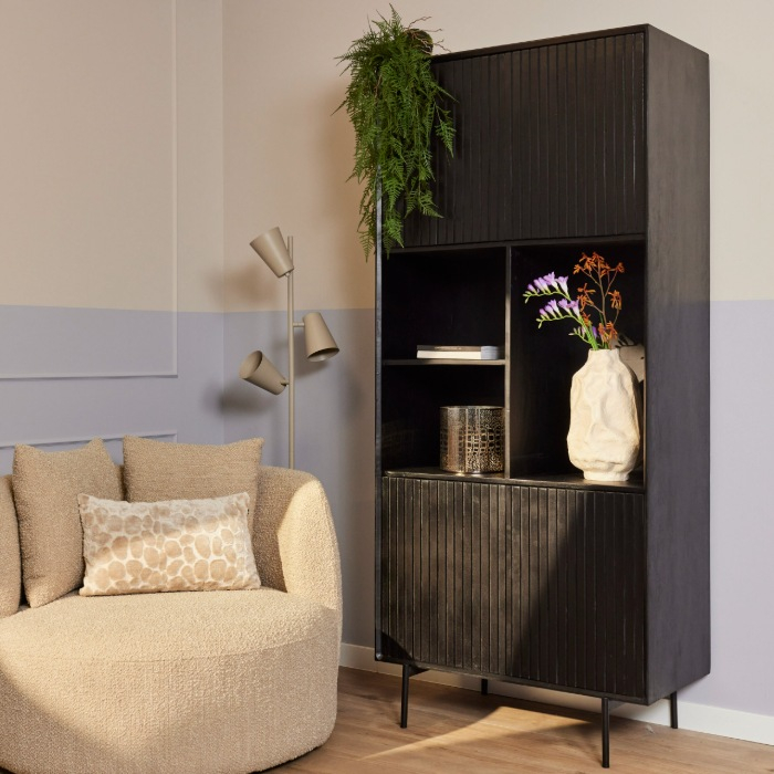 Vakkenkast Madison in zwart mangohout met open vakken naast een fauteuil