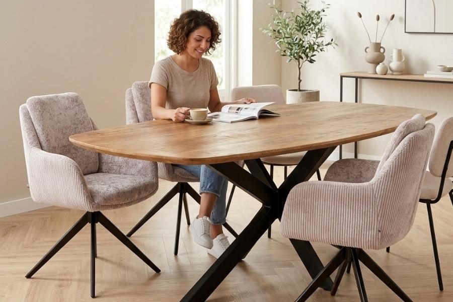 Vrouw leest aan een ovale mangohouten eettafel met ribstof eetkamerstoelen