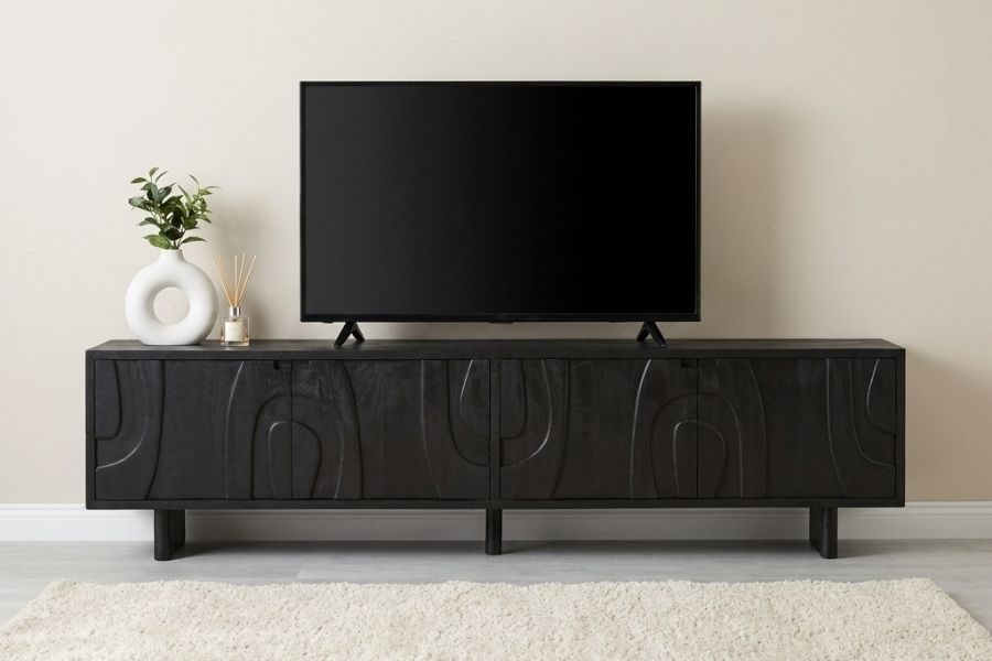 Breed zwart tv-meubel met reliëfdeuren onder een televisie