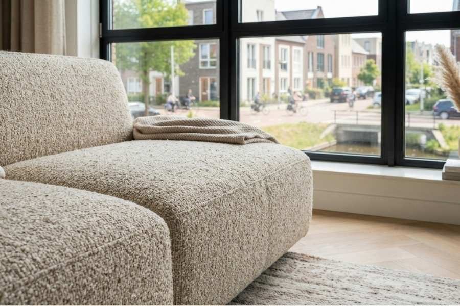 Bouclé hoekbank bij een raam met een plaid over de chaise longue