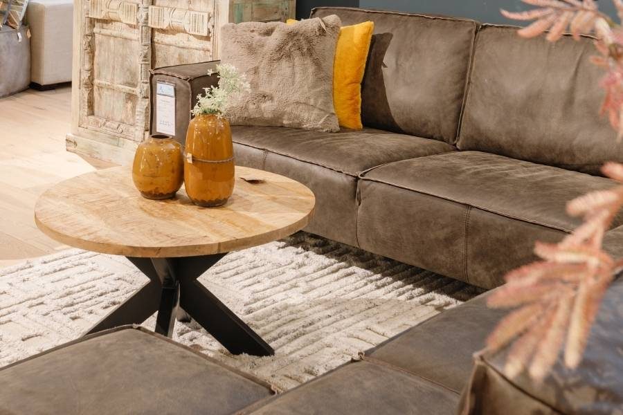 Ronde mangohouten salontafel met zwarte spinpoot bij een leren bank