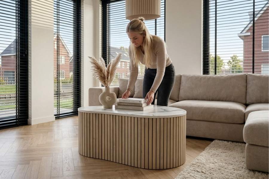 Vrouw stylet een ribbelsalontafel met boeken en een vaas pampasgras