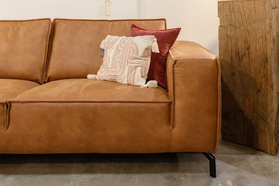 Cognackleurige leren bank met sierkussens tegen een houten wand